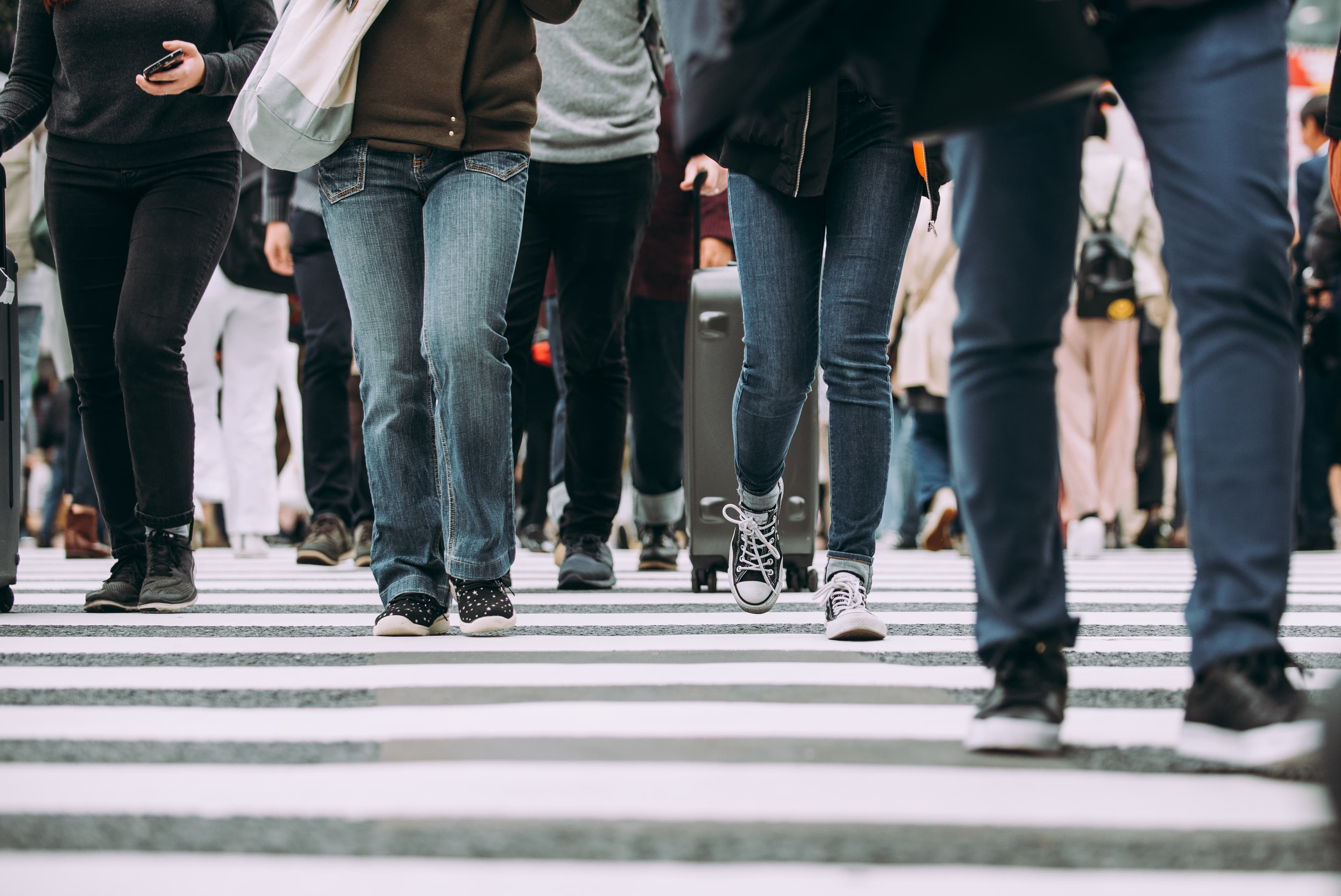 Low-angle view of a dense crowd of people crossing a wide zebra-striped intersection in Tokyo.