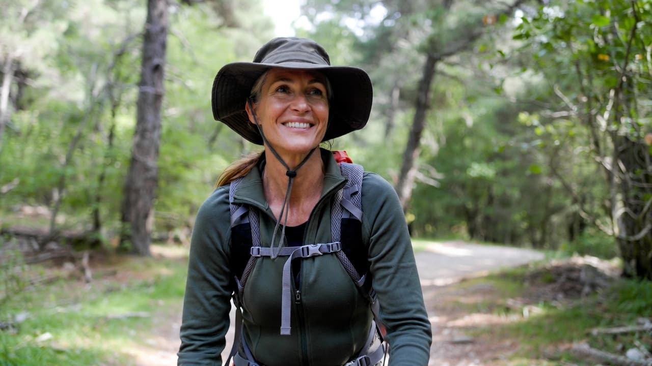 Middle-aged woman smiling while hiking on a wooded trail with a large backpack.