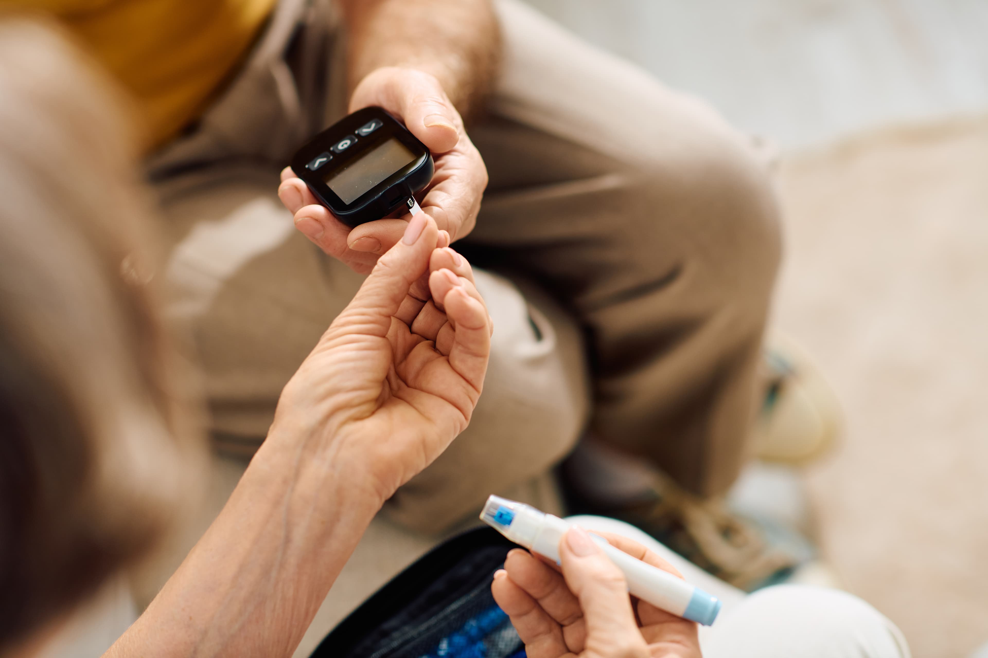 Close-up of a person assisting a senior with a blood glucose meter and lancet device.