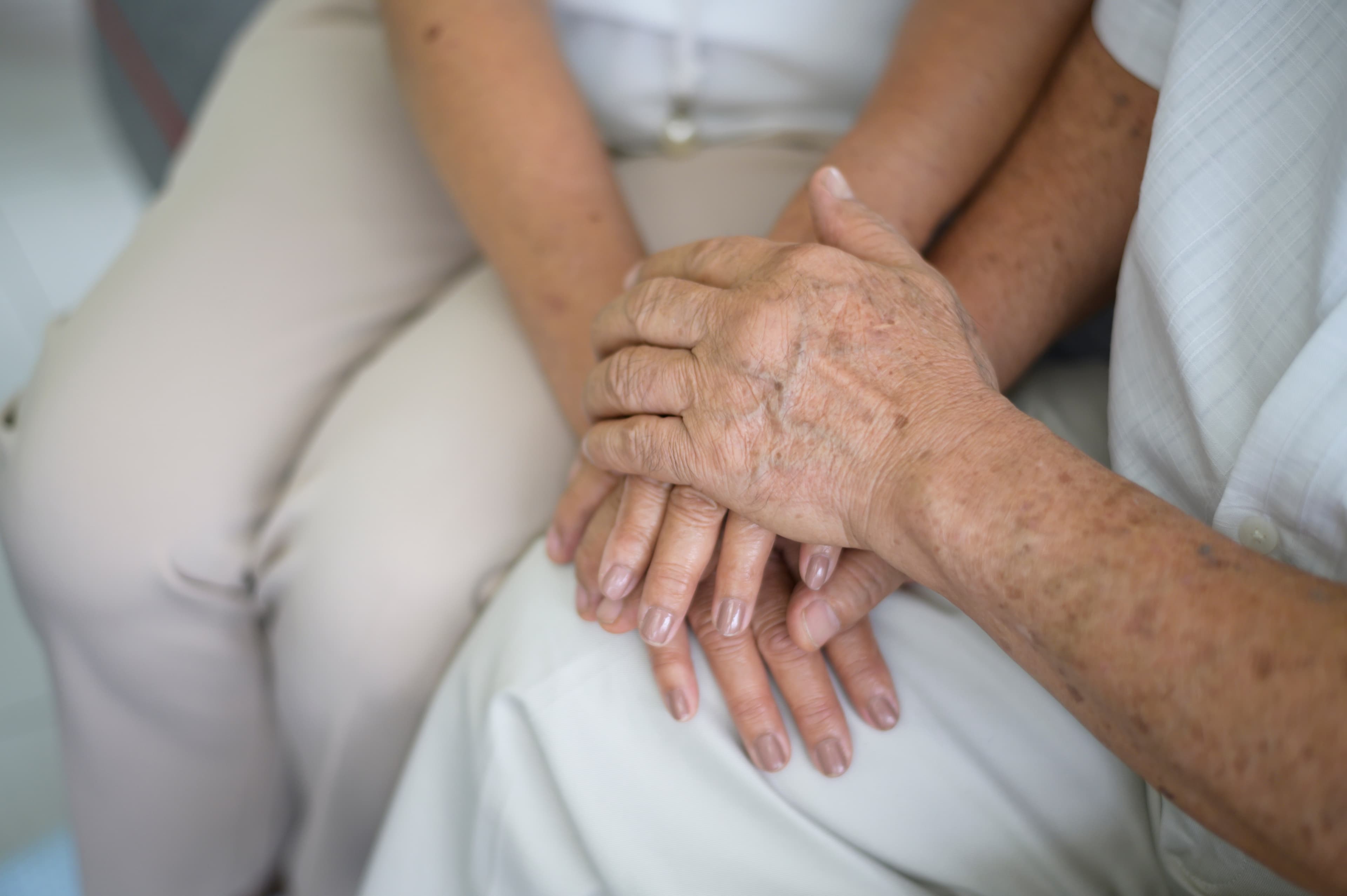 Close-up of younger hands gently holding the aged wrinkled hands of an elderly person.
