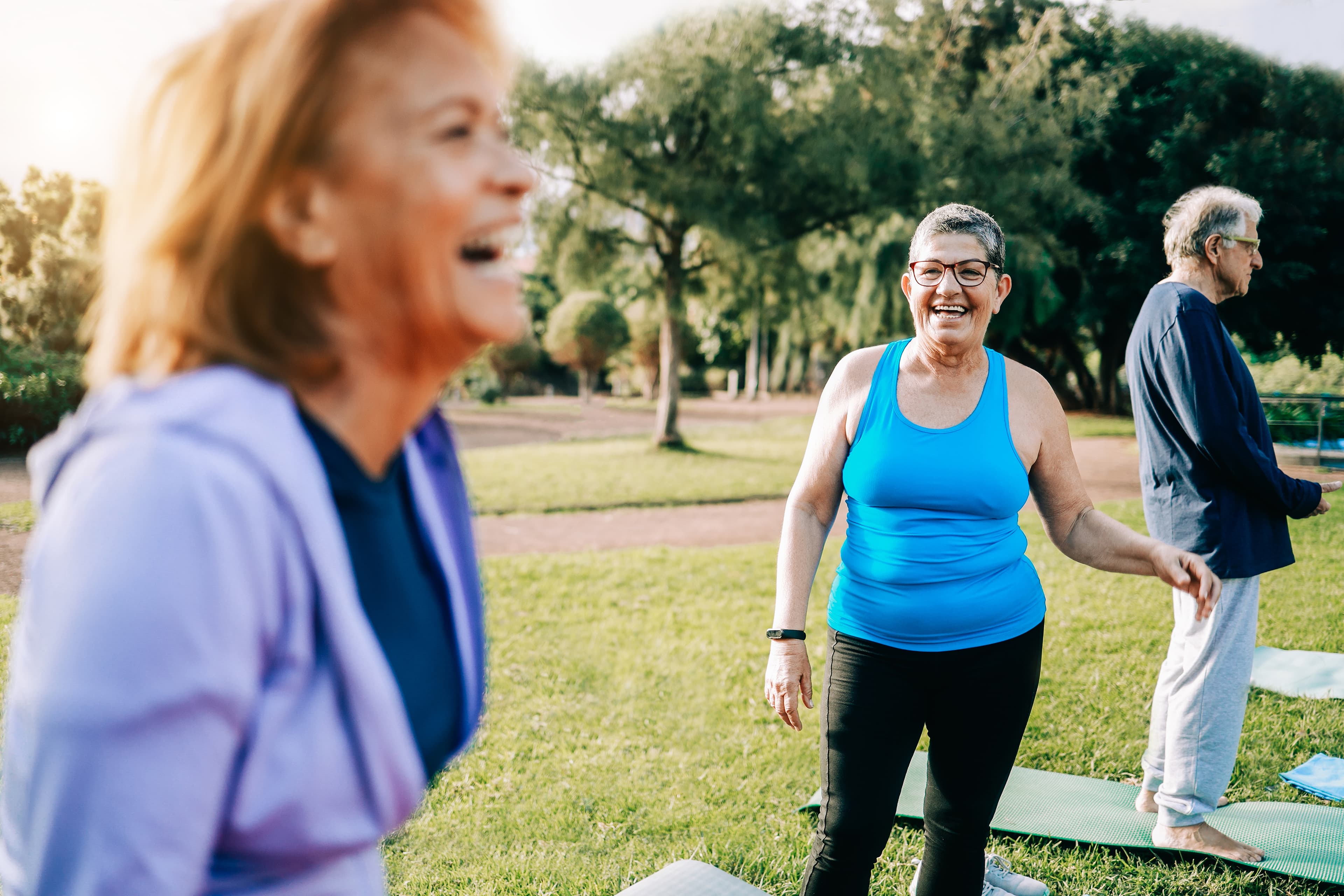 Group of smiling senior adults doing outdoor yoga or exercise class on grass in a park.